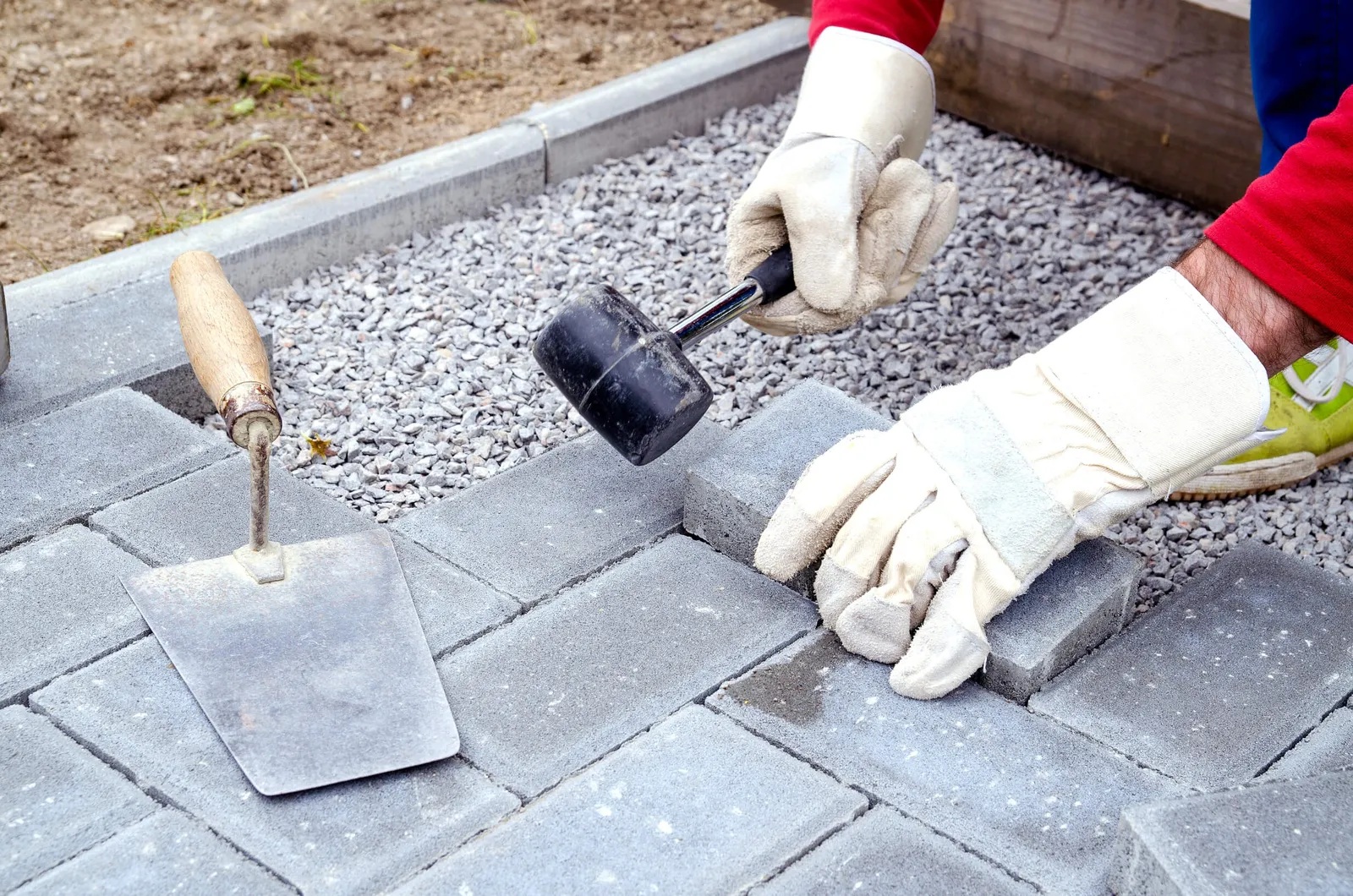 Bricklayer places concrete paving stone blocks for building up a patio, using hammer